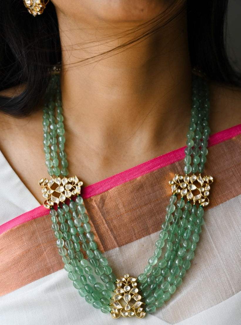 A person wearing a silver and green moissanite pendant mala with intricate designs and earrings.