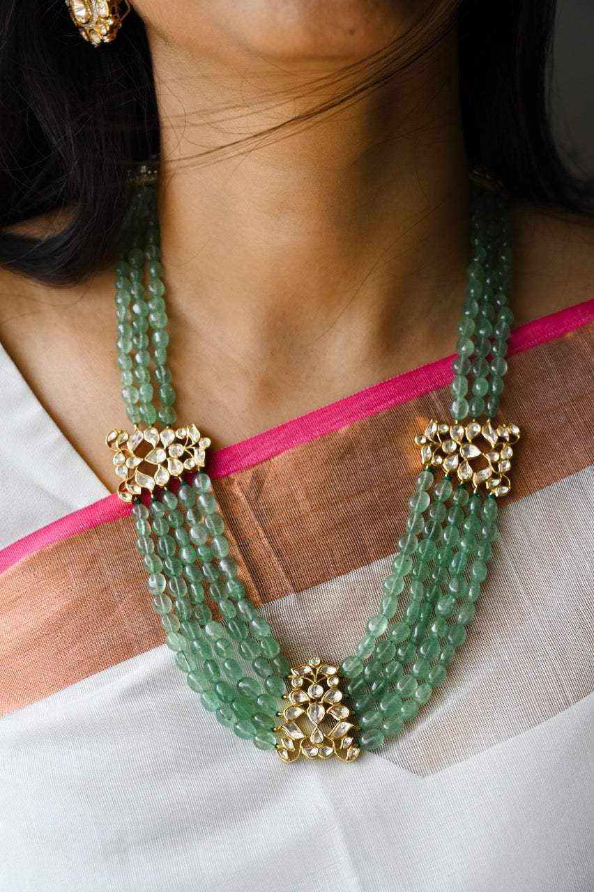 A person wearing a silver and green moissanite pendant mala with intricate designs and earrings.