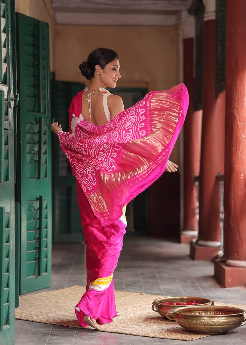 Woman in a bright pink saree with white patterns walking through a doorway.