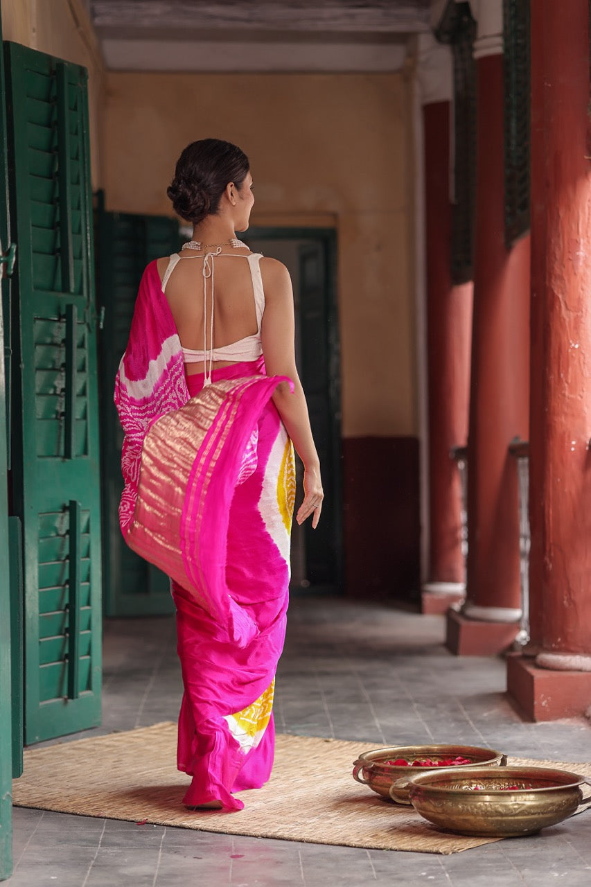 Woman in a bright pink saree walking through a hallway with columns.