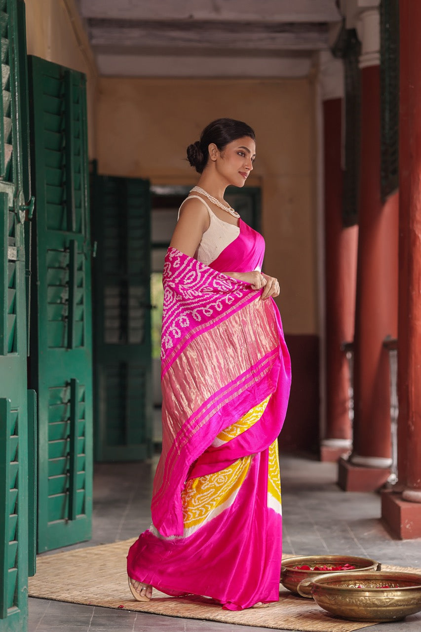 Woman in a bright pink saree with a yellow pattern standing in a traditional setting.