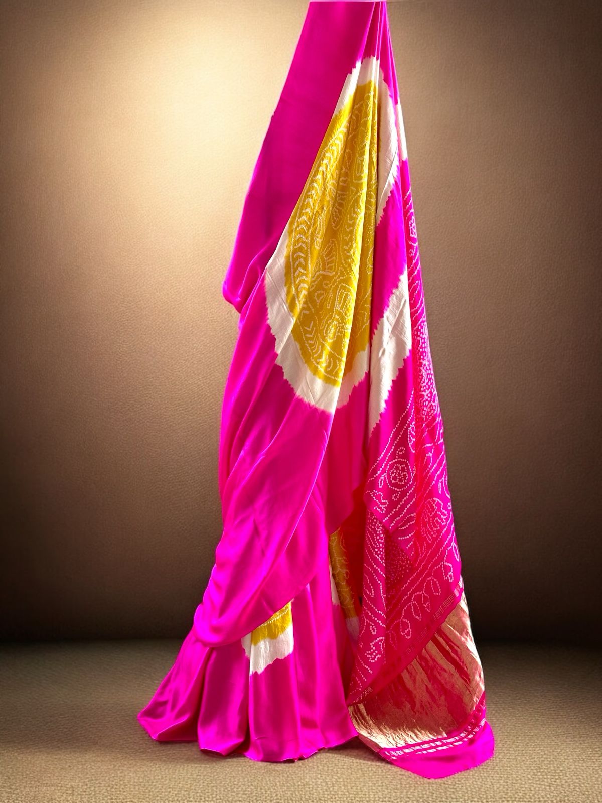A pure Gajji silk pink and yellow bandhani saree draped and displayed, with intricate circle patterns.