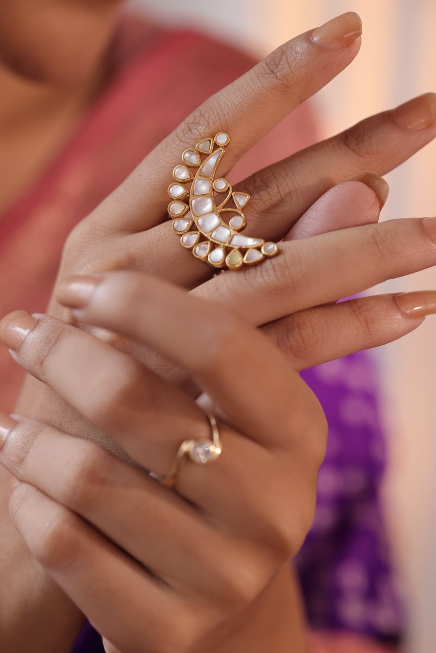 Gold ring with pearl design on a hand against a blurred background