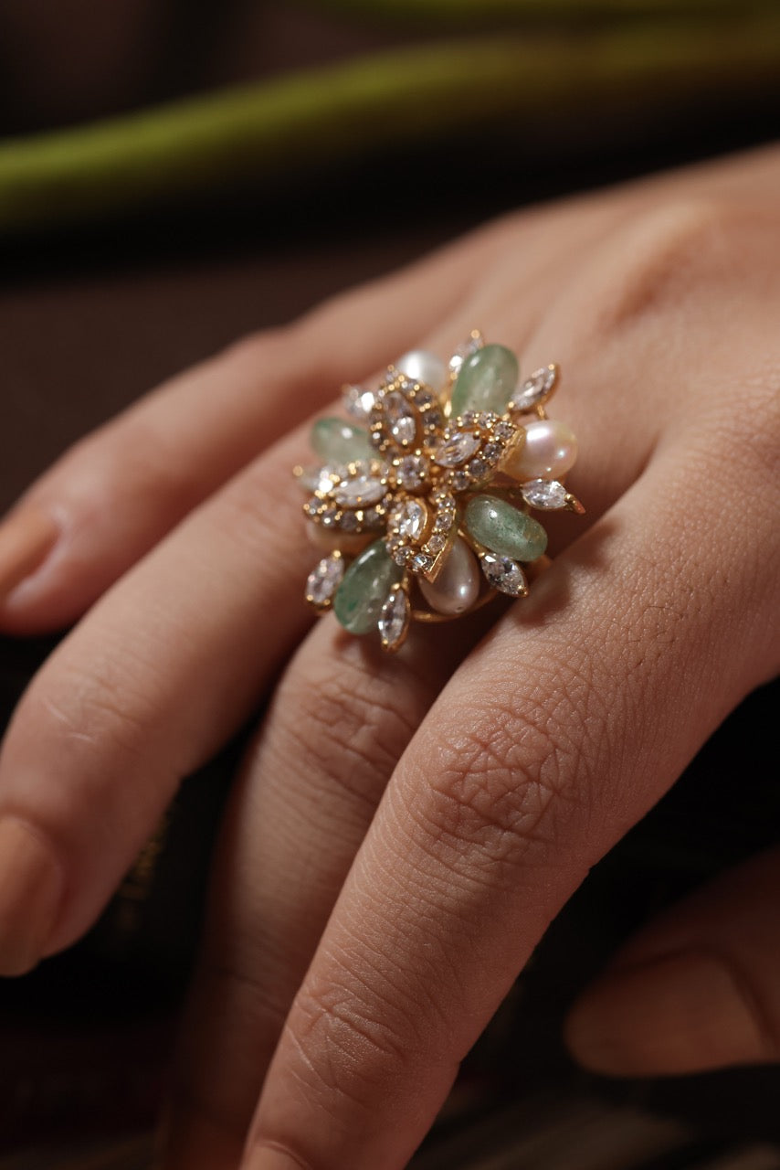 Close-up of a hand wearing a decorative ring with green gemstones and pearls.