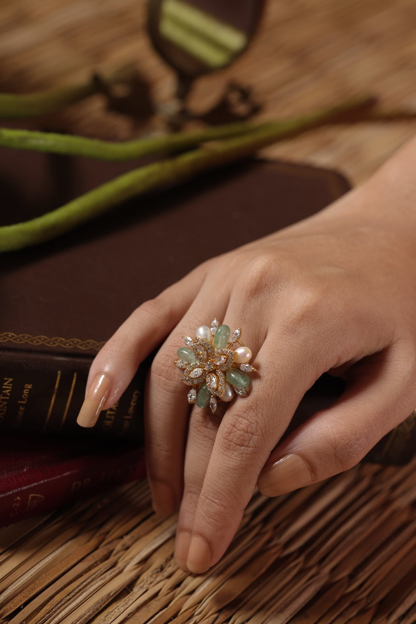Hand wearing a decorative ring on a wooden surface with a book and green fabric in the background