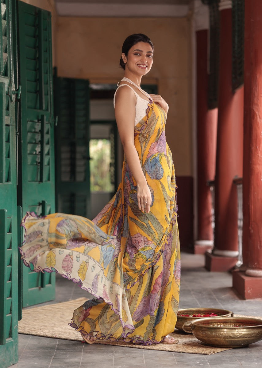 Woman in a colorful saree standing in a traditional setting with green doors and red pillars.