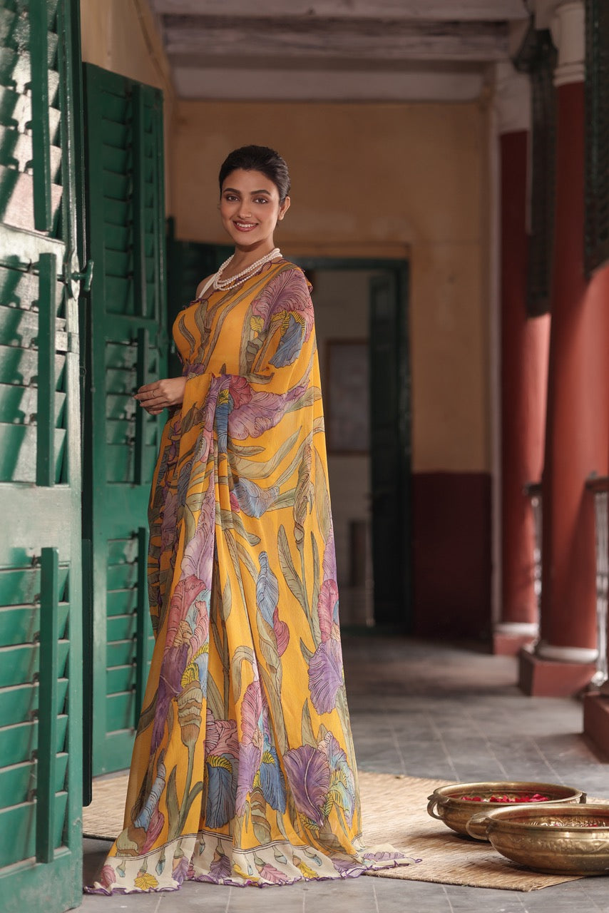 Woman in a yellow saree with floral patterns standing in a traditional setting.