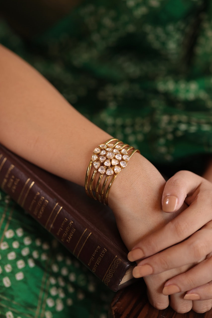 Woman in a green saree holding a cup, sitting on a wooden bench wearing a 92.5 silver handcuff with moissanite polki.