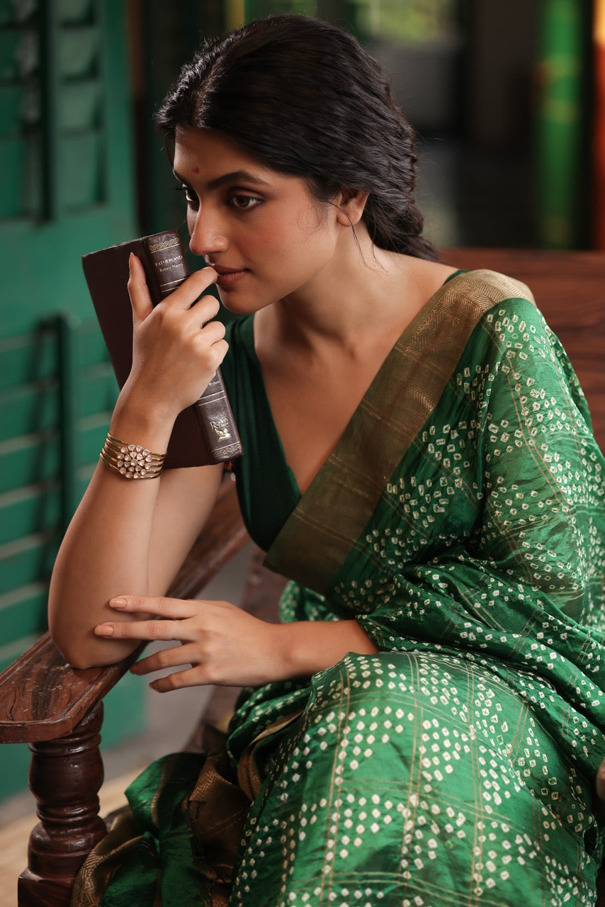 Woman in a green saree holding a cup, sitting on a wooden bench wearing a 92.5 silver handcuff with moissanite polki.