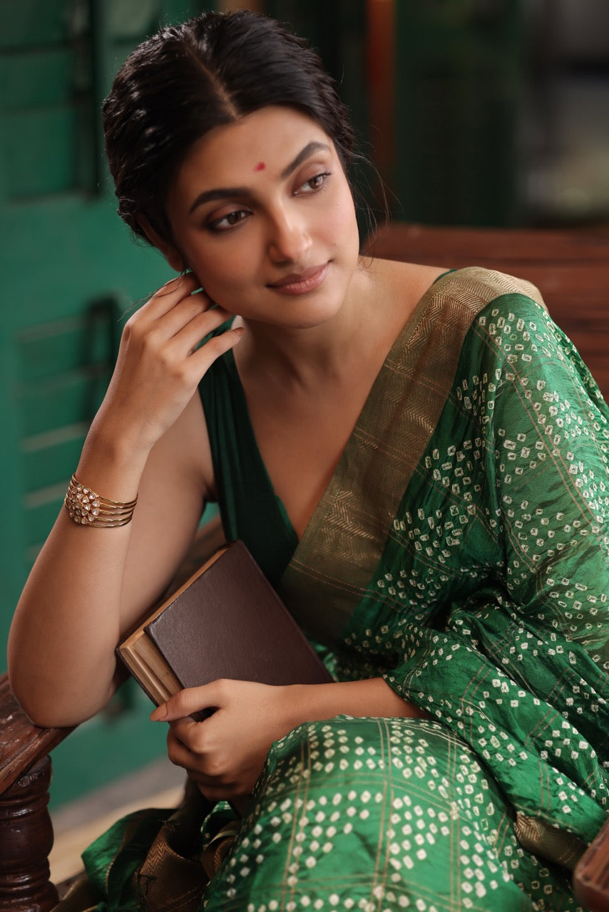 Woman in a green saree holding a cup, sitting on a wooden bench wearing a 92.5 silver handcuff with moissanite polki.