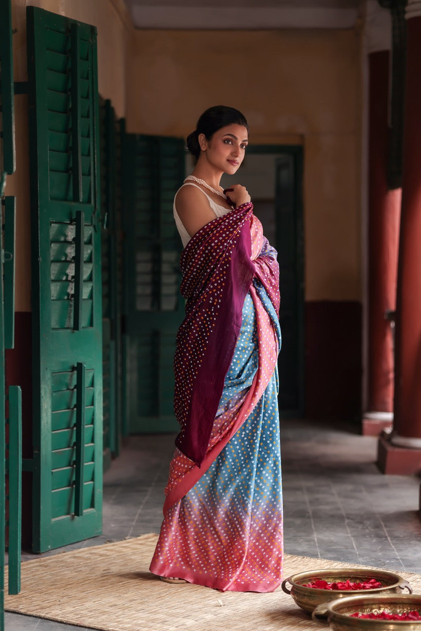 Woman in a colorful saree standing in a room with green shutters and a textured floor.