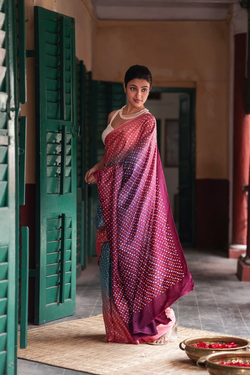 Woman in a colorful saree standing in a room with green shutters and a textured floor.