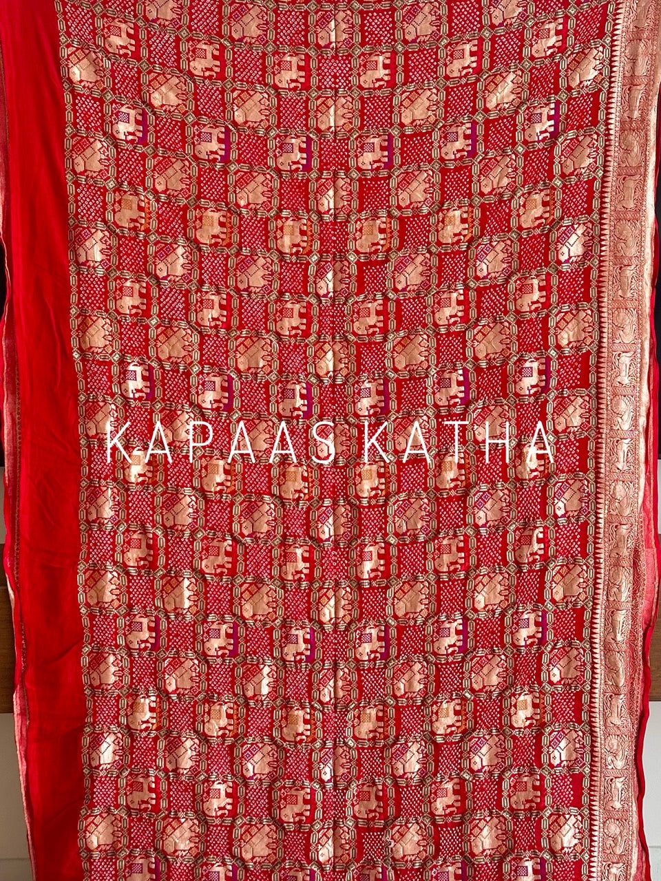 Buy pure Banarasi georgette Bandhani saree in vermilion red with gold zari elephant motifs & rich woven pallu. Authentic handloom luxury online at Kapaas Katha.
