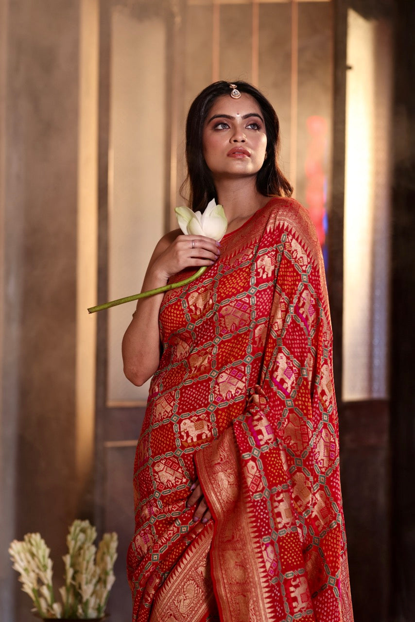 Buy pure Banarasi georgette Bandhani saree in vermilion red with gold zari elephant motifs & rich woven pallu. Authentic handloom luxury online at Kapaas Katha.