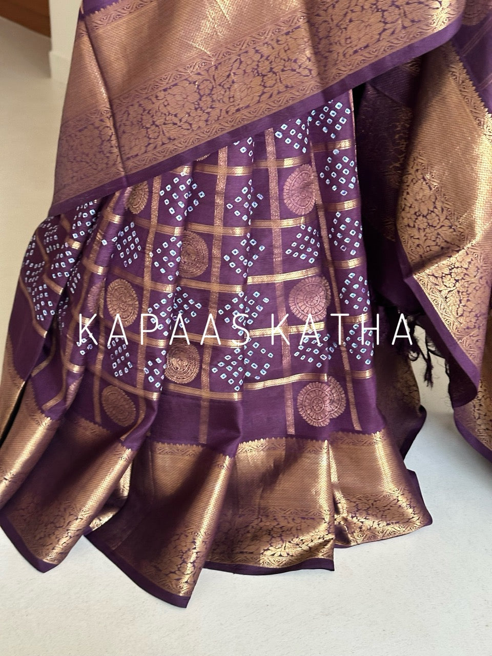 Buy pure Vasundhara silk Bandhani saree in plum purple with gold zari checks & rich pallu. Authentic handwoven luxury online at Kapaas Katha.