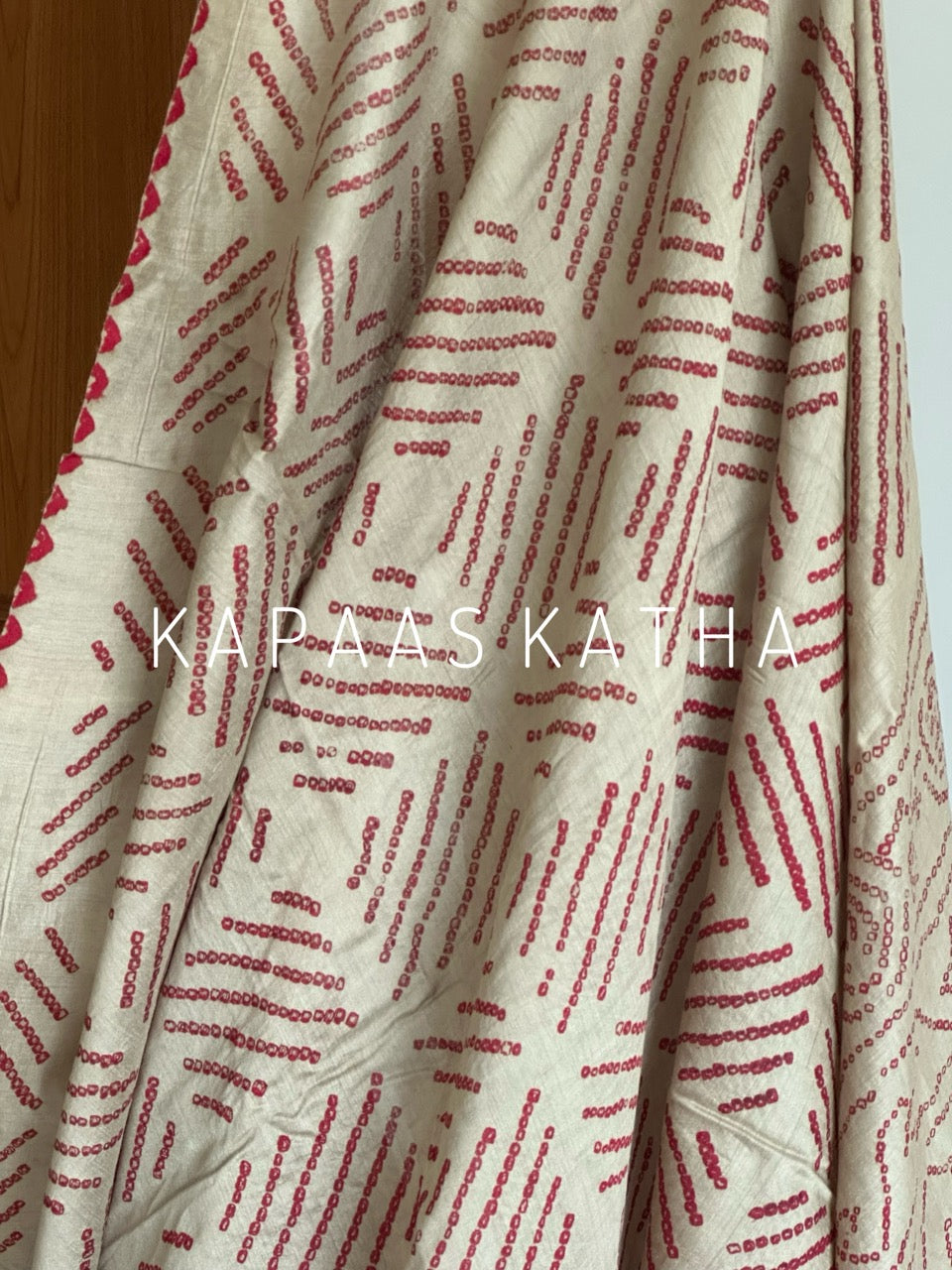 Buy pure Munga silk Bandhani saree in linen beige with soft red ghangura border. Lightweight handloom elegance for daytime festivities at Kapaas Katha.