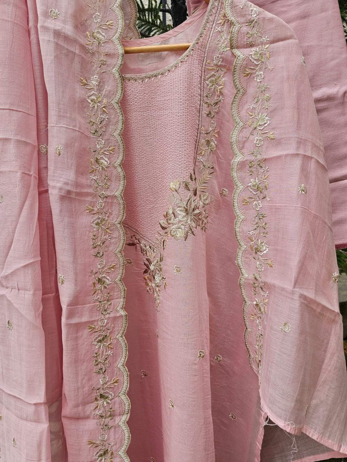 A light pink 3-piece Chanderi Mulmul semi-stitched suit set with floral embroidery, displayed on a hanger.