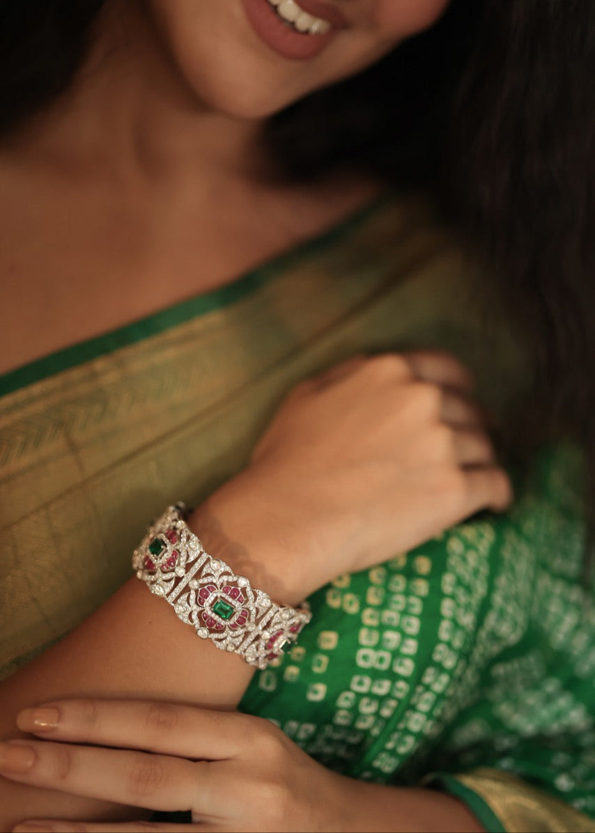 Woman wearing a green saree with a silver bracelet featuring red and green stones.