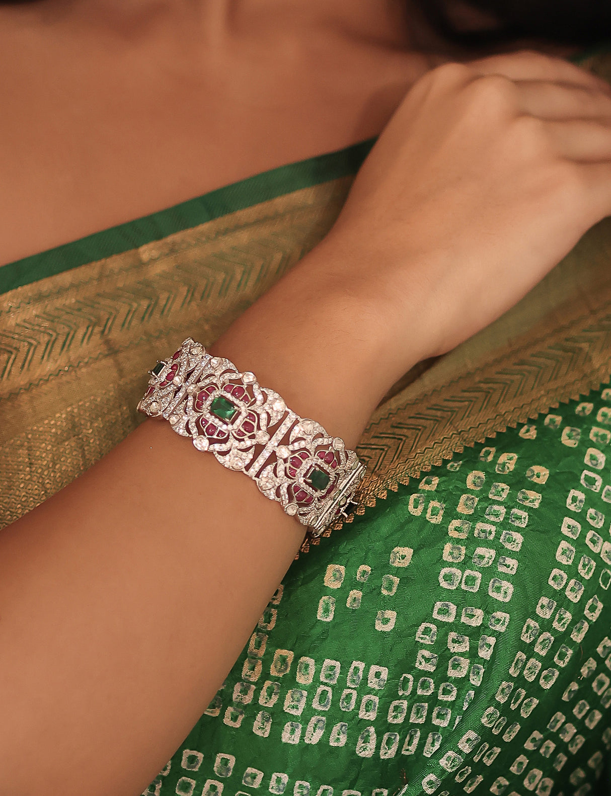 Silver bracelet with green gemstones on a wrist, against a green saree background