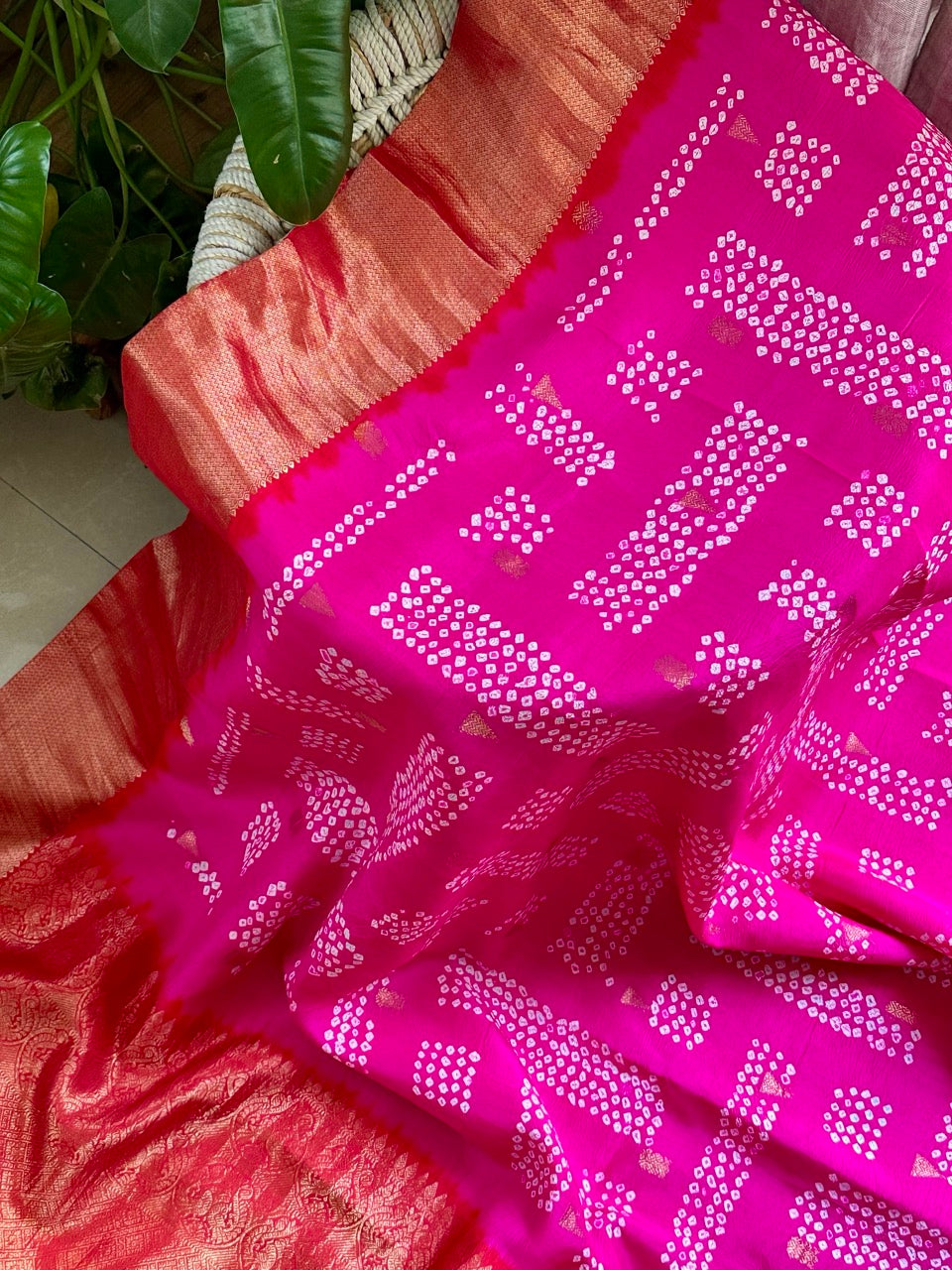 A rolled-up image of a red and pink Kanchipattu Bandhani saree with a geometric grid pattern and zari border detailing.