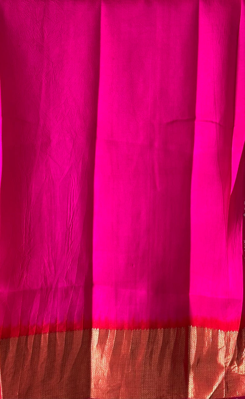 A rolled-up image of a red and pink Kanchipattu Bandhani saree with a geometric grid pattern and zari border detailing.