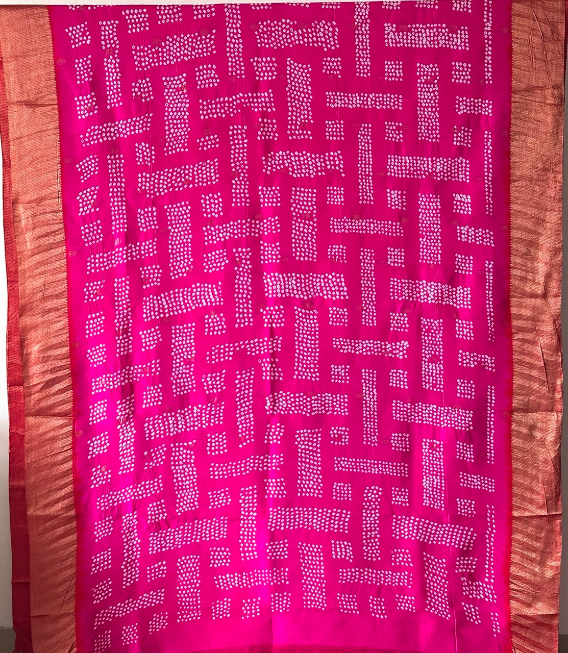 A rolled-up image of a red and pink Kanchipattu Bandhani saree with a geometric grid pattern and zari border detailing.