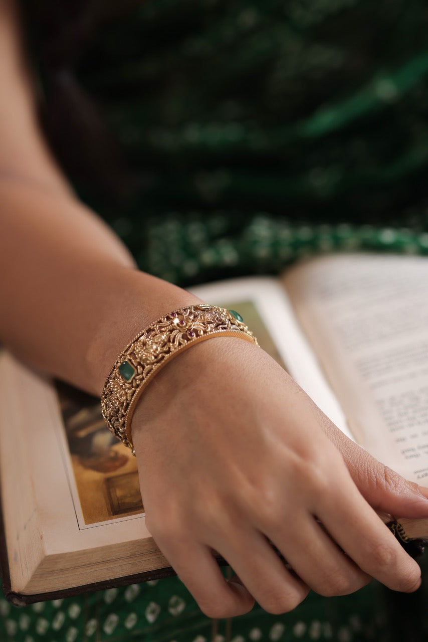 Hand wearing a 92.5 silver kada with green stones on an open book