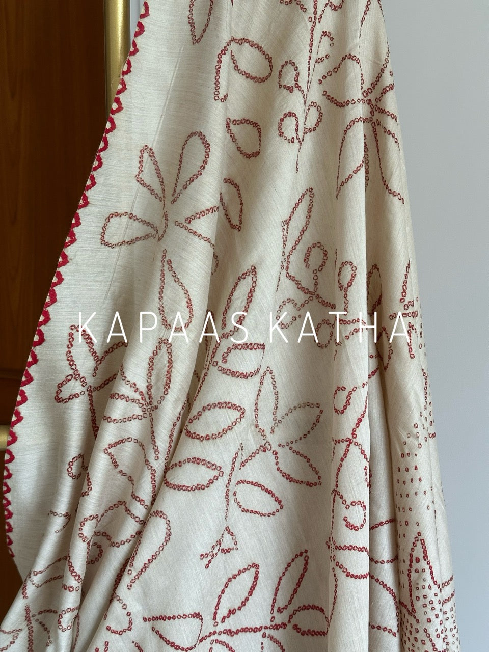 Buy pure Munga silk Bandhani saree in linen beige with soft red ghangura border. Lightweight handloom elegance for daytime festivities at Kapaas Katha.