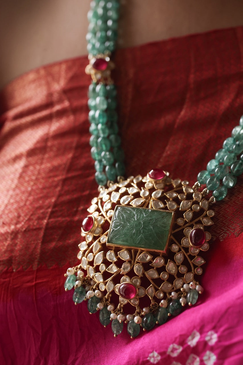 Close-up of a decorative necklace with a green stone on a red fabric background