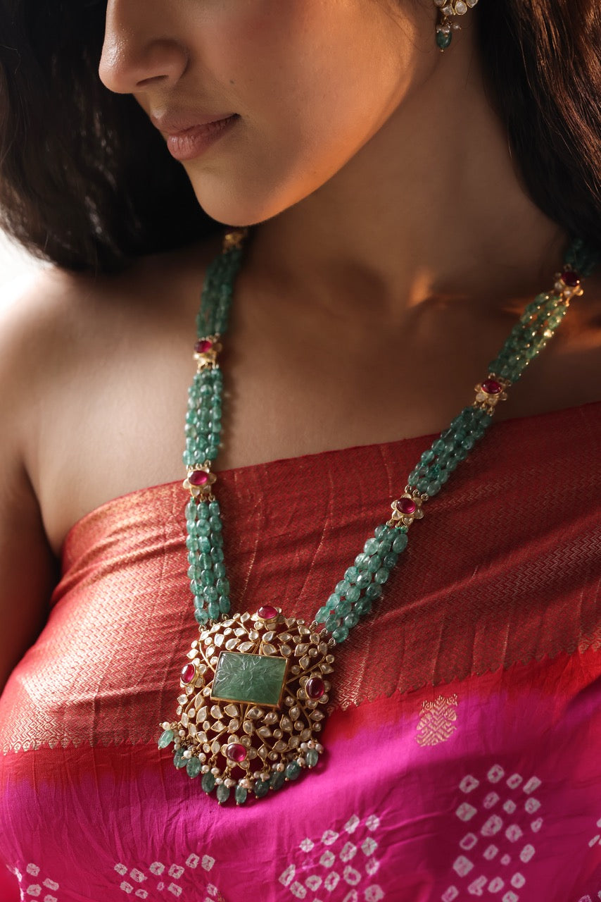 Woman wearing a traditional necklace and earrings, dressed in a red and pink saree.
