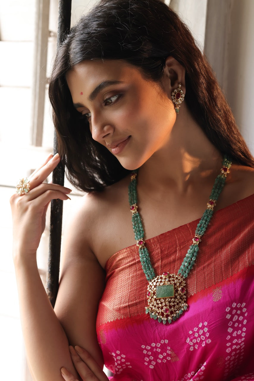 Woman wearing a red saree with a green necklace indoors