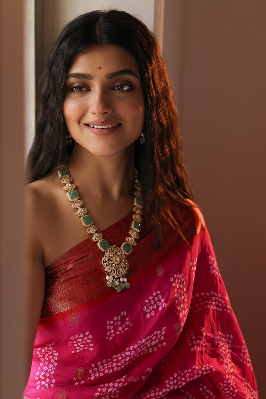 Woman wearing a red saree with a floral pattern and a prominent necklace against a neutral background