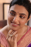 Woman wearing a ring with a decorative design, set against a blurred indoor background.