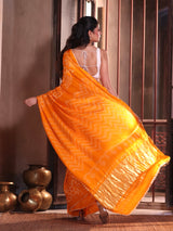 Woman in an orange saree with a white blouse standing in a room with decorative pots.