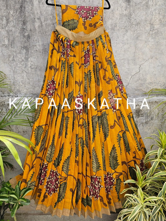 Yellow floral dress on a hanger with 'Kapaaskatha' branding against a gray textured wall.