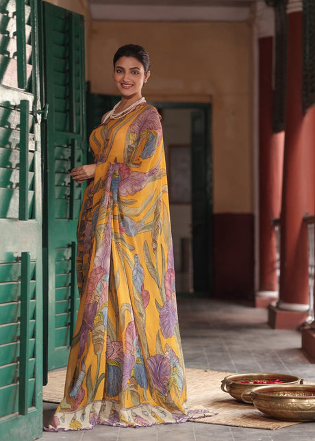 Woman in a yellow saree with floral patterns standing in a traditional setting.