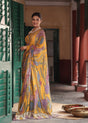 Woman in a yellow saree with floral patterns standing in a traditional setting.
