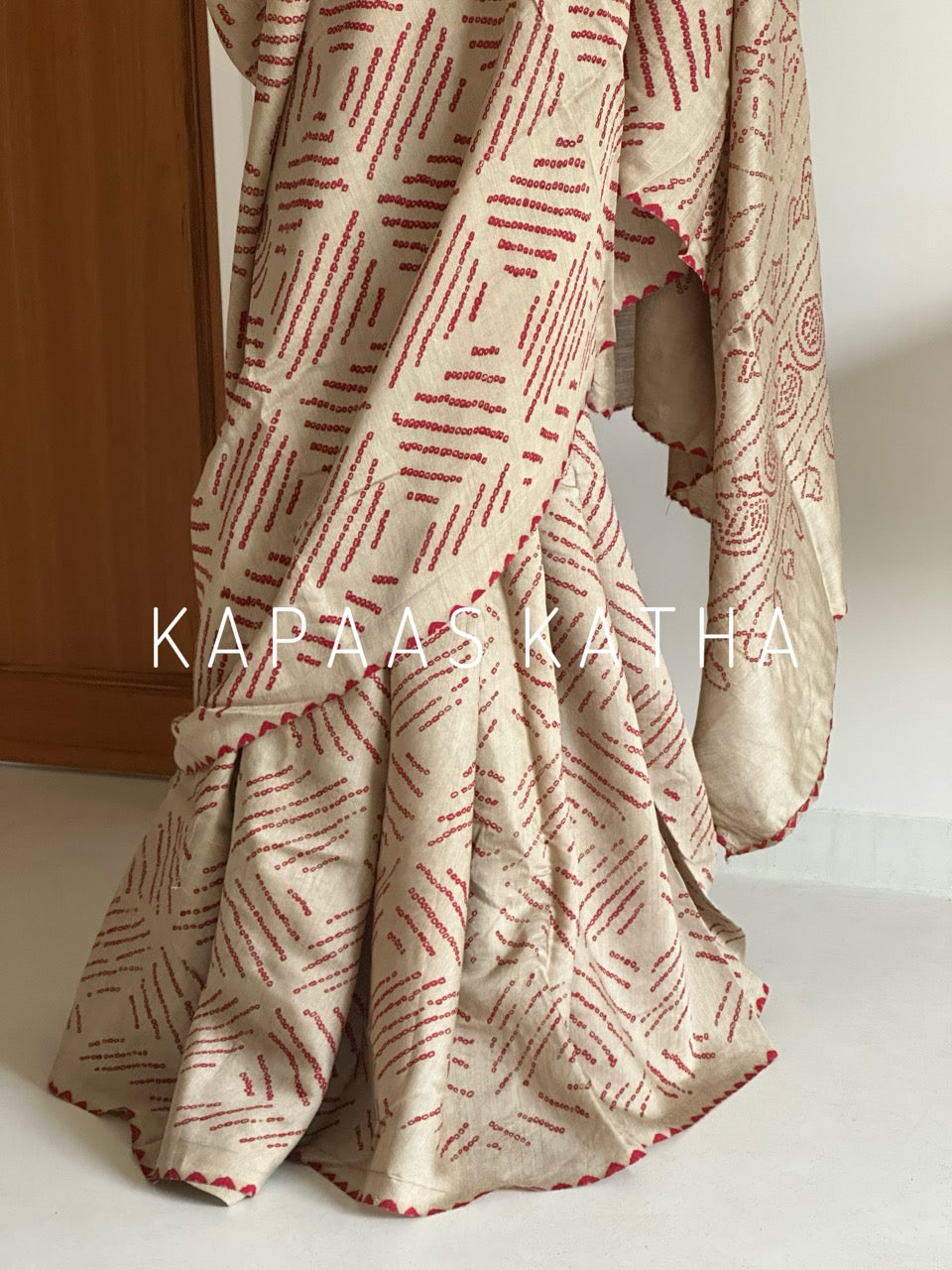 Buy pure Munga silk Bandhani saree in linen beige with soft red ghangura border. Lightweight handloom elegance for daytime festivities at Kapaas Katha.