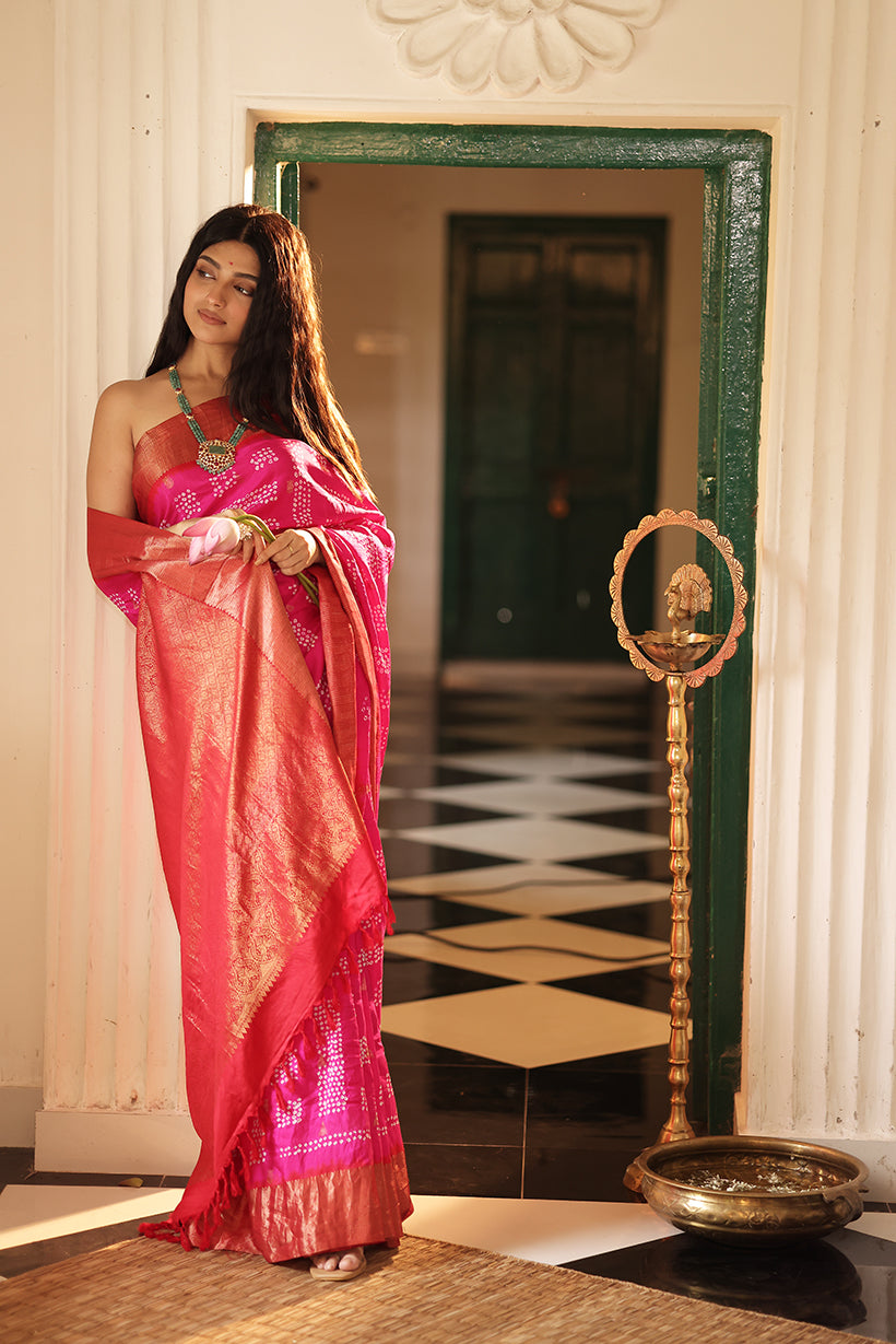 Woman in a pink saree standing in a room with a mirror and decorative items.