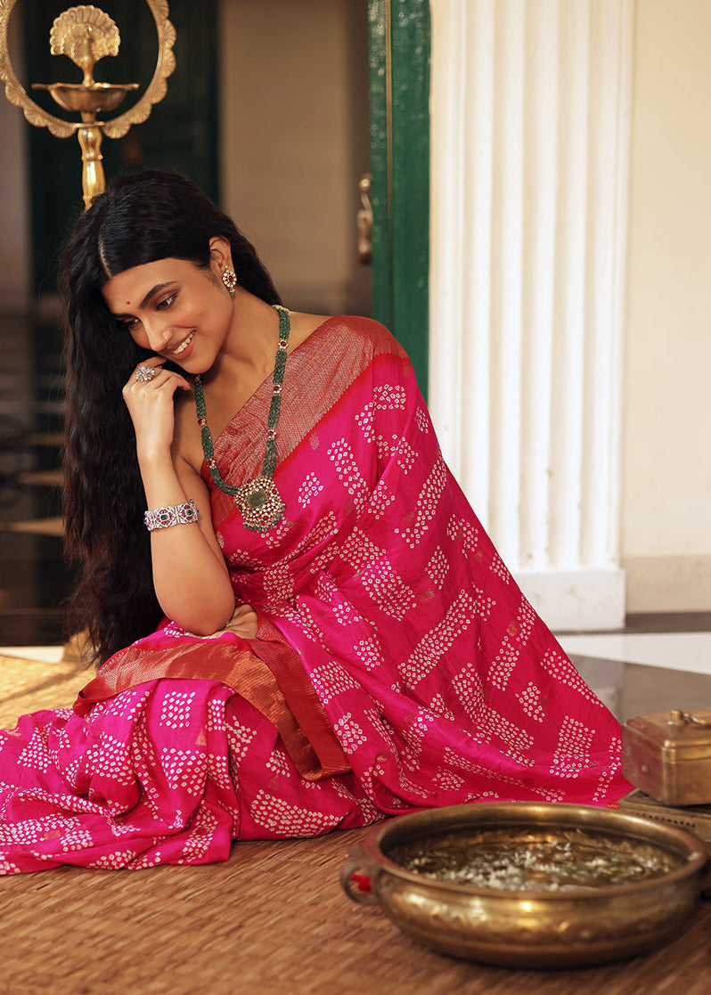 Woman in a pink saree sitting on a wooden floor with a decorative background