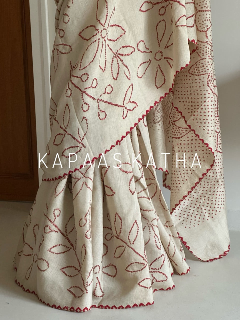 Buy pure Munga silk Bandhani saree in linen beige with soft red ghangura border. Lightweight handloom elegance for daytime festivities at Kapaas Katha.