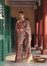 Woman in a colorful saree standing in an outdoor setting with architectural elements.