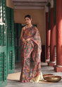 Woman in a colorful saree standing in an outdoor setting with architectural elements.