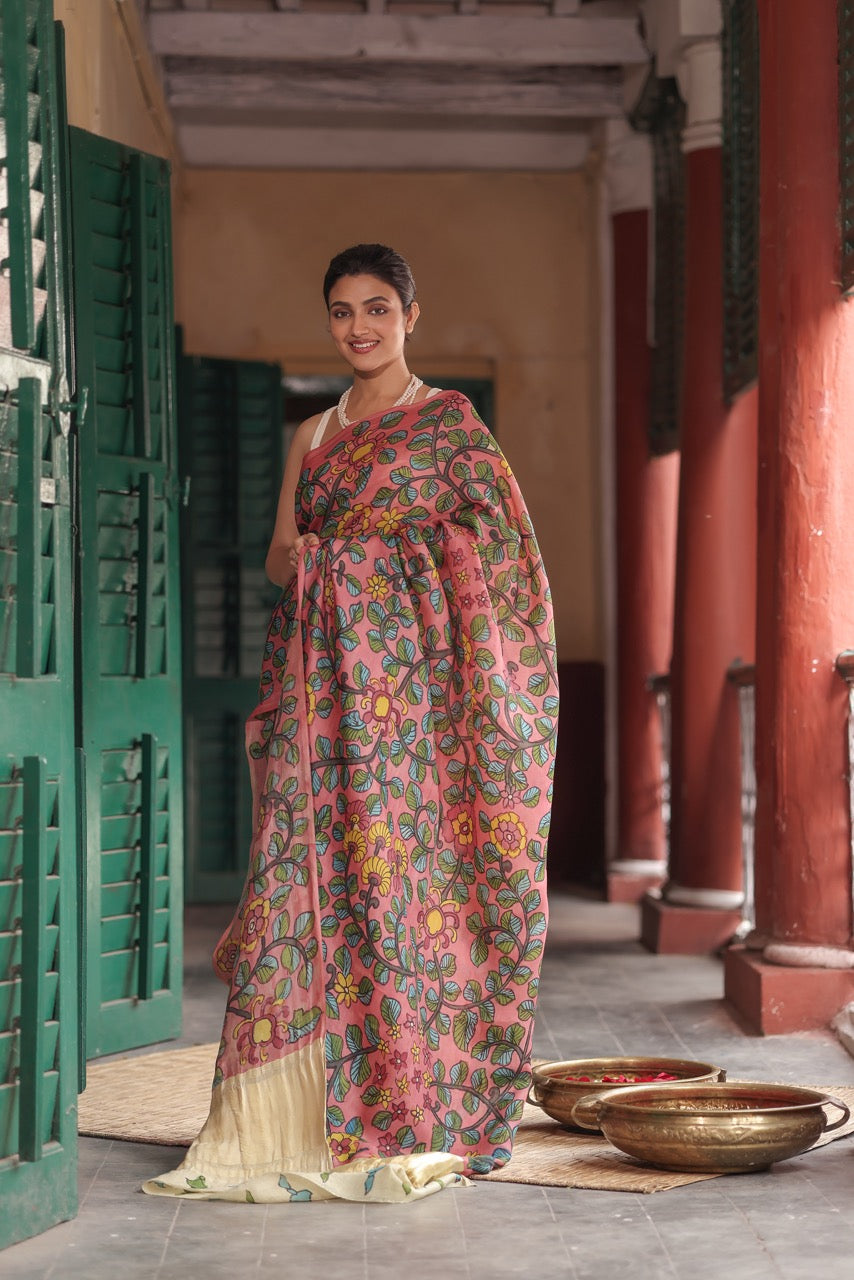 Woman in a floral saree standing in an indoor setting with traditional decor.