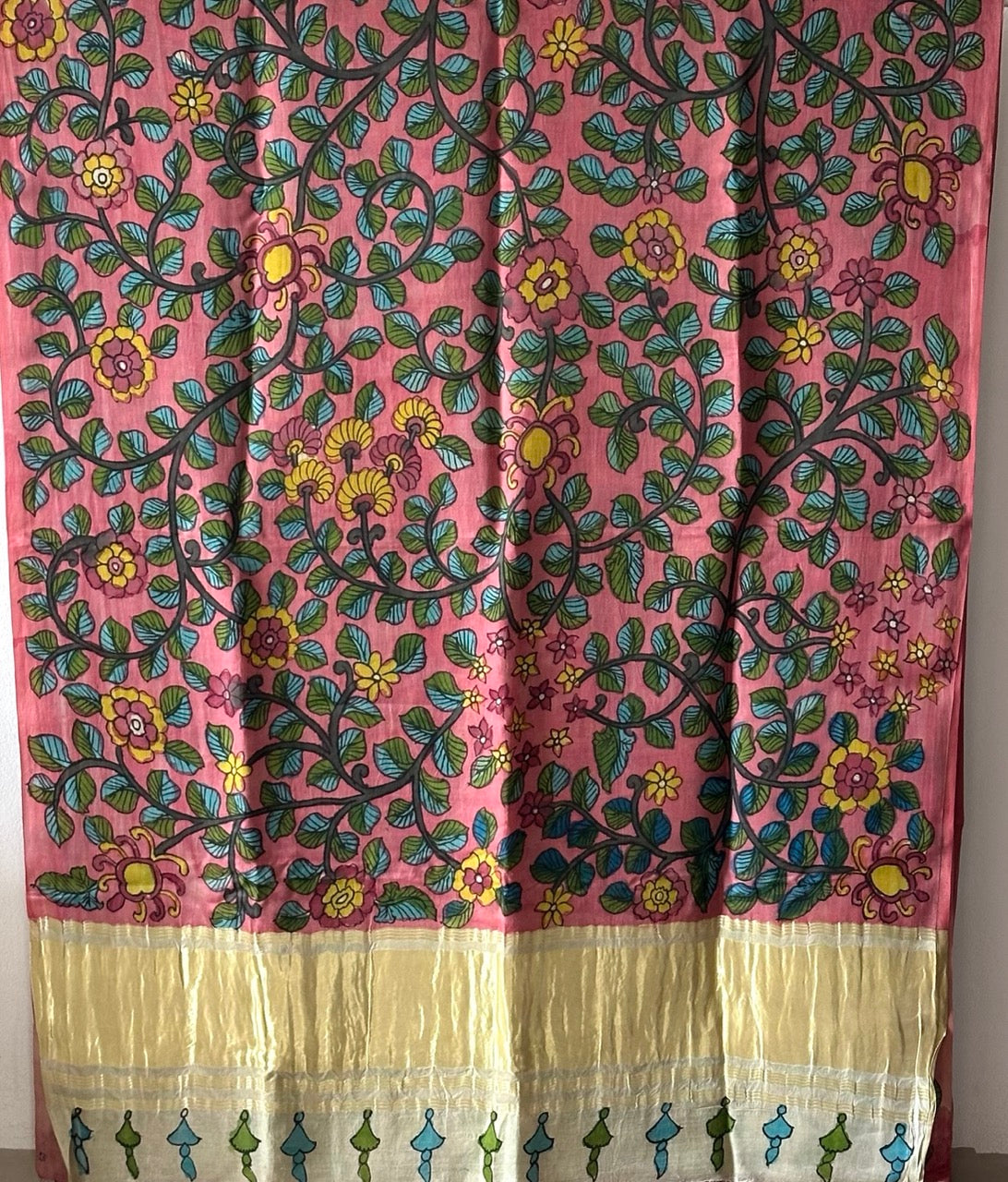 Woman in a floral saree standing in an indoor setting with traditional decor.